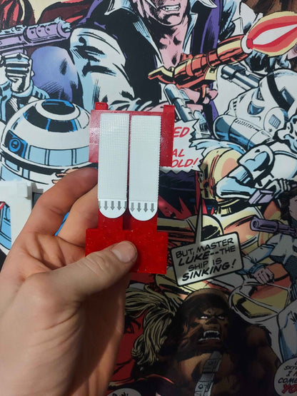 Hand holding the specialised glossy red mounting bracket with two white detachable heavy-duty adhesive strips.