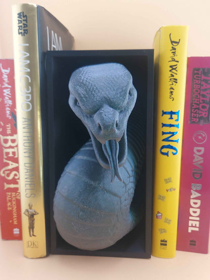 Symmetrical front view of the colour-shift snake emerging from the book nook, positioned between several colourful books.