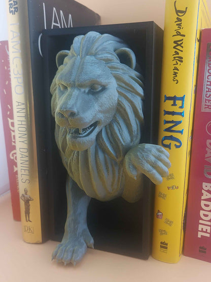 Low angle view of the textured, snarling green-grey lion bookend gripping the yellow and red books tightly.