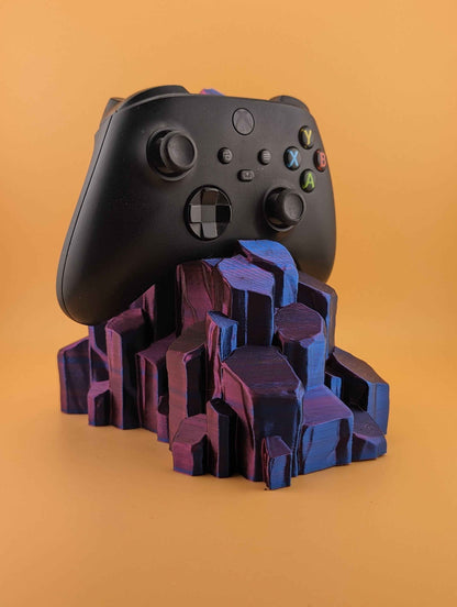 Front view of a black Xbox controller perched on a stand made of faceted crystals in deep purple and vibrant pink-blue.
