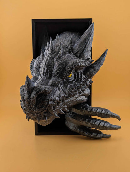 Textured grey dragon bust displaying large horns and claws. The head pushes out of a black square box against an orange background.