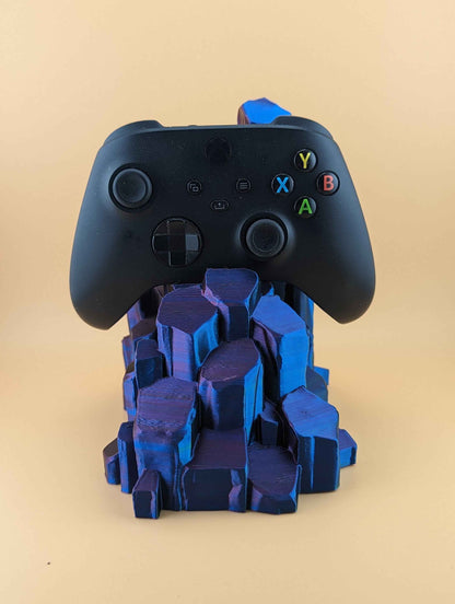 Centred view of a black controller held by a large rock formation stand featuring dark blue and subtle indigo facets.