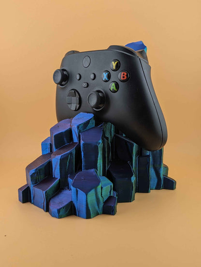Black Xbox controller resting on a rocky stand, shifting from deep blue to bright teal crystal facets.