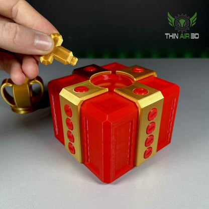 Close up view of a hand inserting the small gold cross-shaped key into the centre mechanism of the red and gold puzzle box lid.