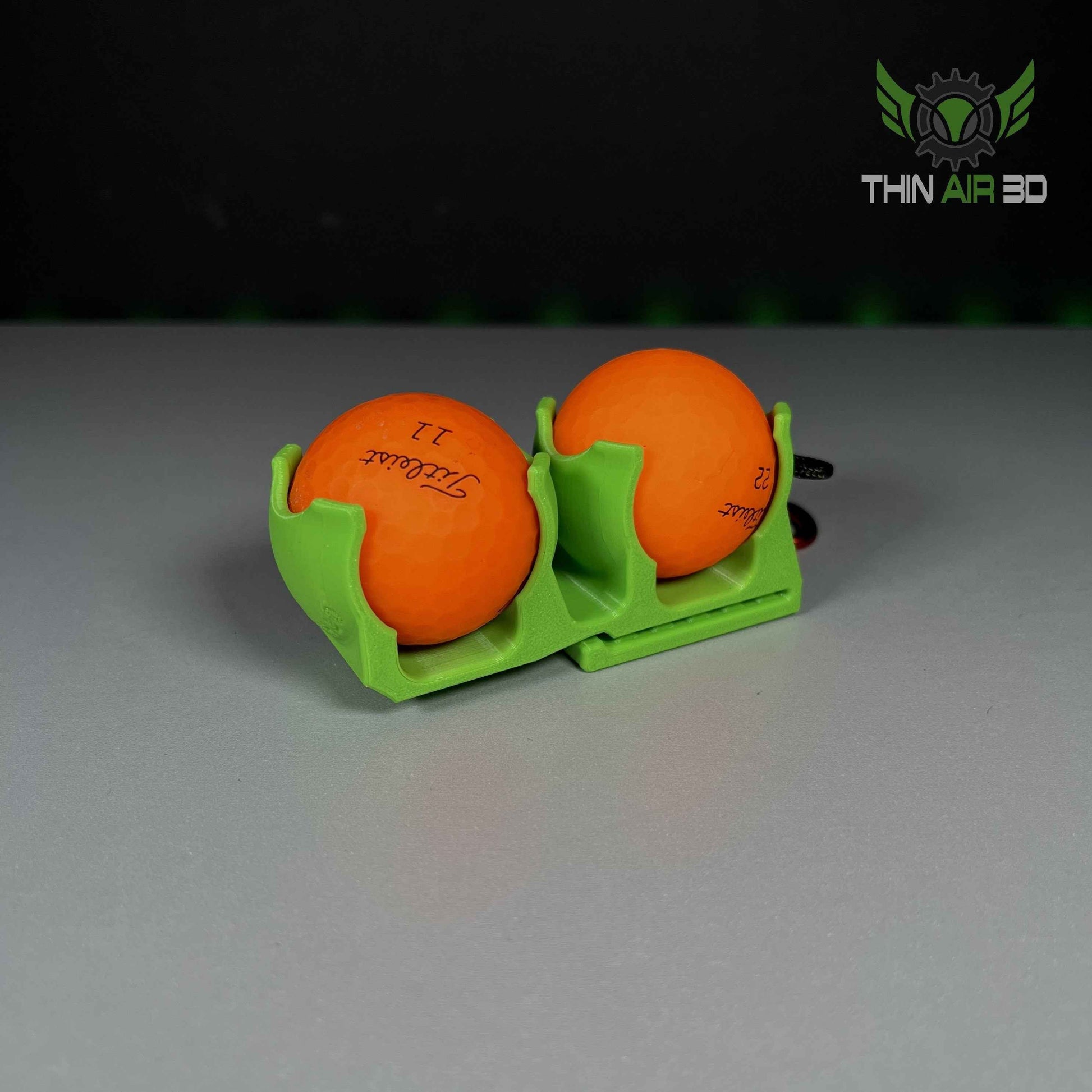 Two orange Titleist golf balls in a connected, double-pocket lime green storage caddy.