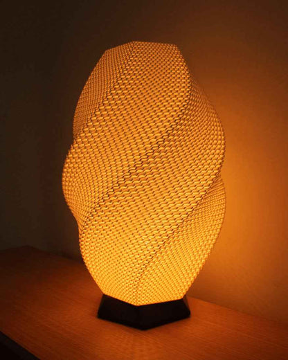 Warm glowing orange, twisted geometric lamp with a tight basket-weave texture, standing on a black hexagonal base.