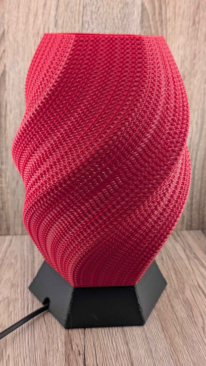 Unlit, vibrant red twisted geometric lamp on a black hexagonal base. The rigid surface displays a continuous, complex wavy texture.
