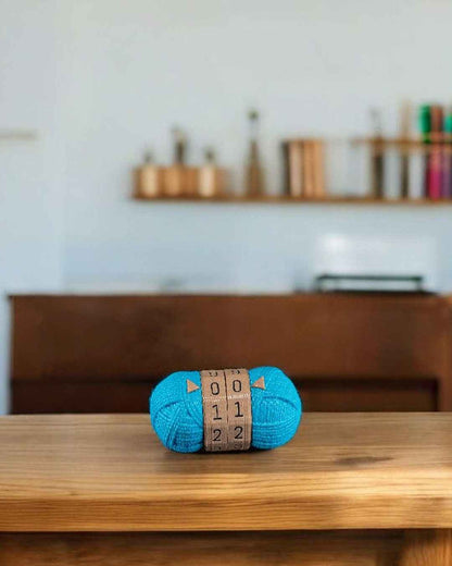 Bright teal yarn counter fidget on a wooden table. Centre dial band shows 00, 11, 22 against a blurred home background.