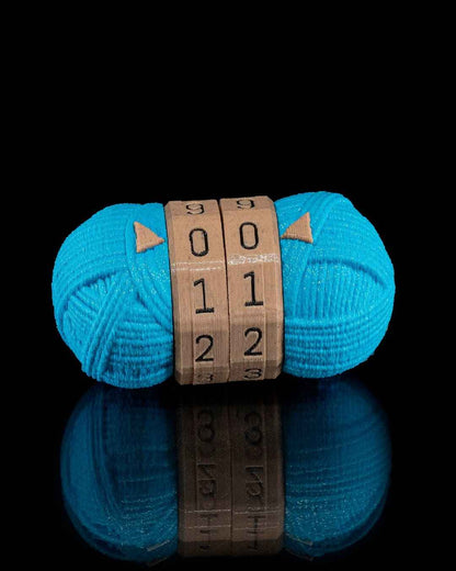 Straight-on view of the teal yarn counter fidget on a reflective black surface. The brown centre dials read 00, 11, 22.