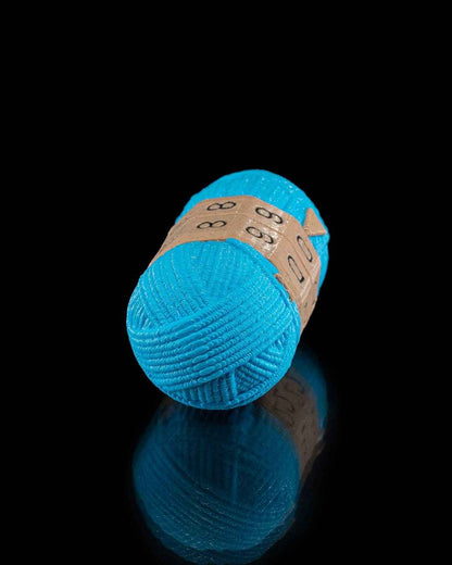 Angled view of the bright teal yarn fidget counter on a black reflective surface. The texture closely mimics coiled knitting yarn.