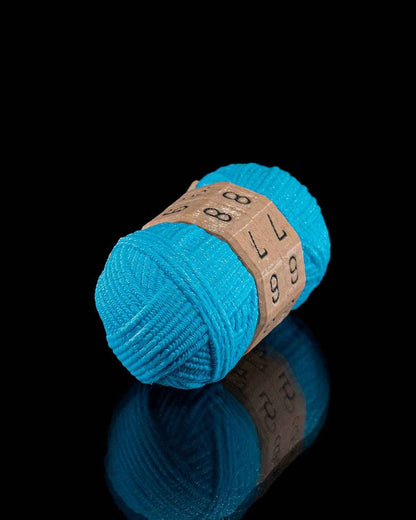 Highly angled close-up of the teal yarn fidget counter detail, resting on a black reflective base. Dials show 88, 77, 66.