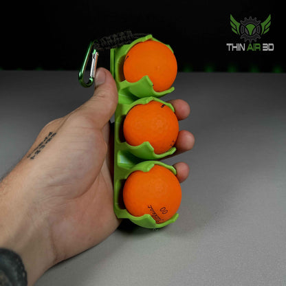 Overhead view of a hand gripping the lime green three-ball carrier, loaded with three bright orange golf balls.