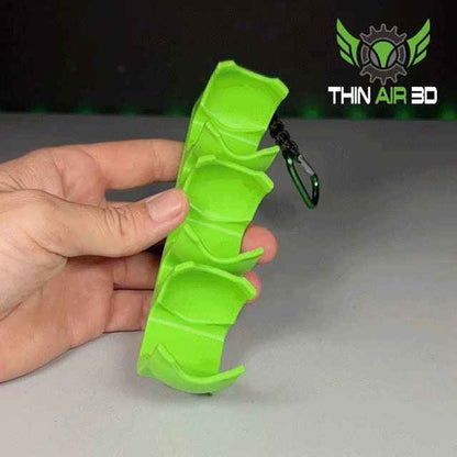 A hand holds the empty, curved, lime green three-pocket ball caddy attached to a black and green carabiner.