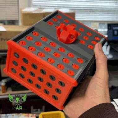 Matte black and red modular container held in a hand, showing the top surface covered in multiple recessed red oval accents.