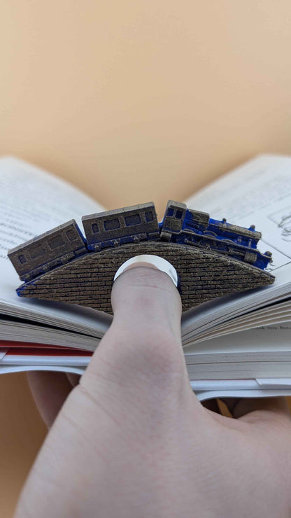 Side view of the train bridge book holder in use; a finger is inserted through the ring to keep the book open.