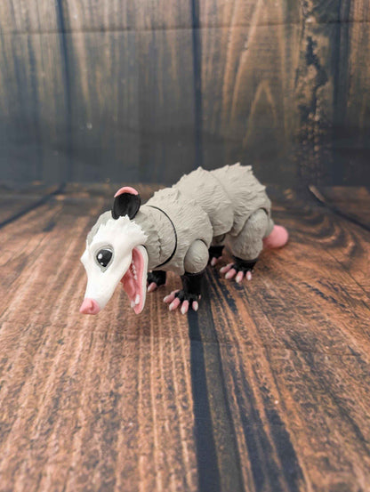 Frontal low-angle view of the grey opossum figurine standing, mouth wide open in a snarl or hiss.