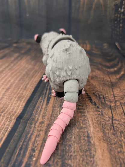 Rear view showing the grey textured body fur and the segmented, flexible pink tail extending outward.