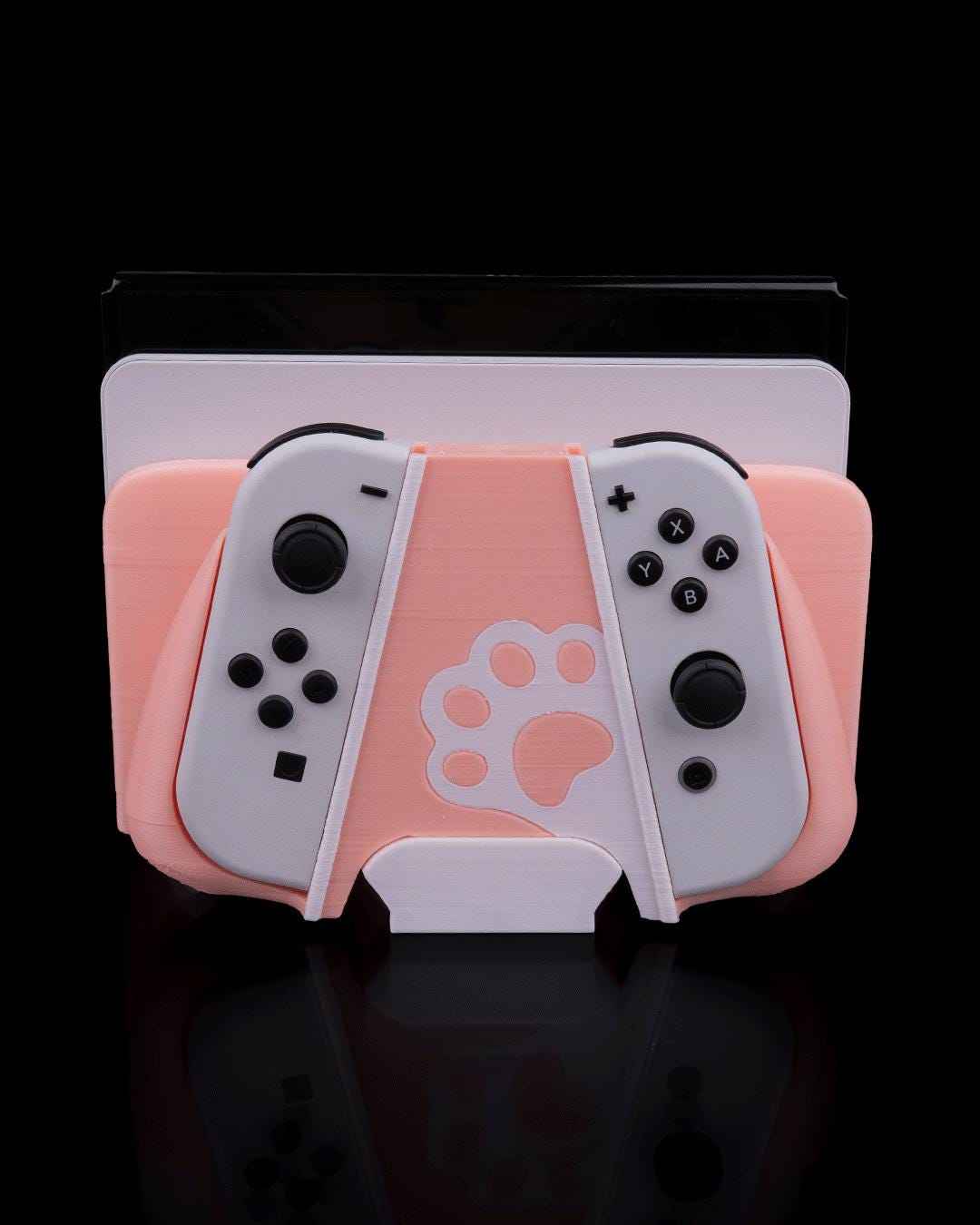 Front view of the matte peach and white cat-themed Nintendo Switch controller dock. Large white paw print centered.