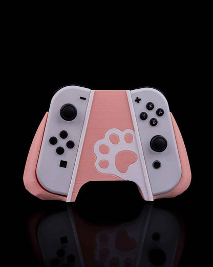 Front view of a two-tone pale pink and white controller grip featuring a paw print cutout, holding two grey Joy-Cons.