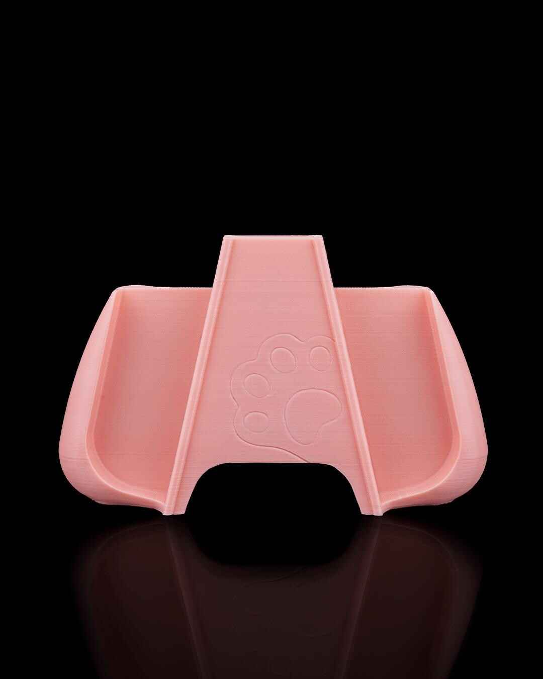 Front view of the empty pale pink controller grip frame, showing the recessed handle openings and central support with a paw print.