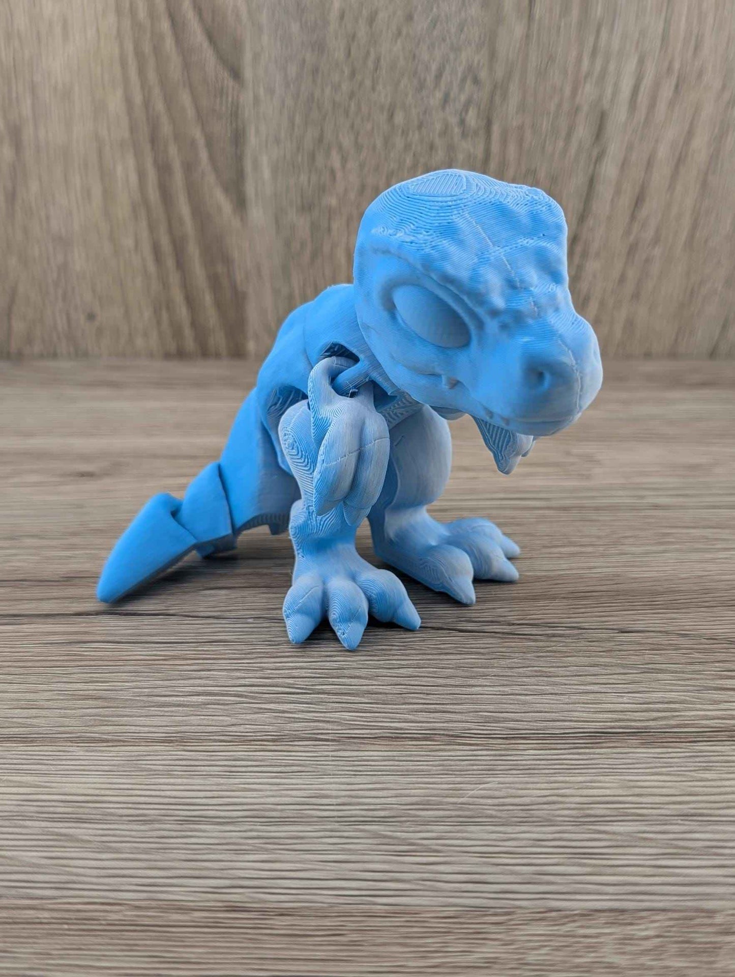 Dynamic three-quarter view of the matte blue T-Rex fidget toy, head turned slightly to the right.