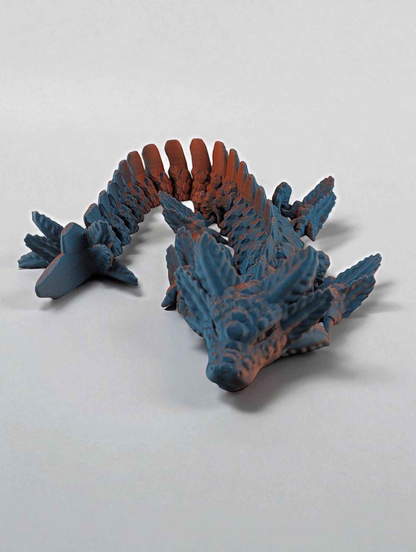 Articulated dragon figure coiled, featuring a rough blue texture that transitions to burnt orange coloration along the spine.
