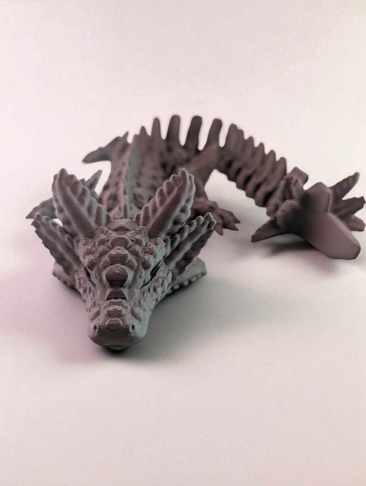 Matte articulated dragon figure, front-facing view, showing spiny crest and segmented tail.