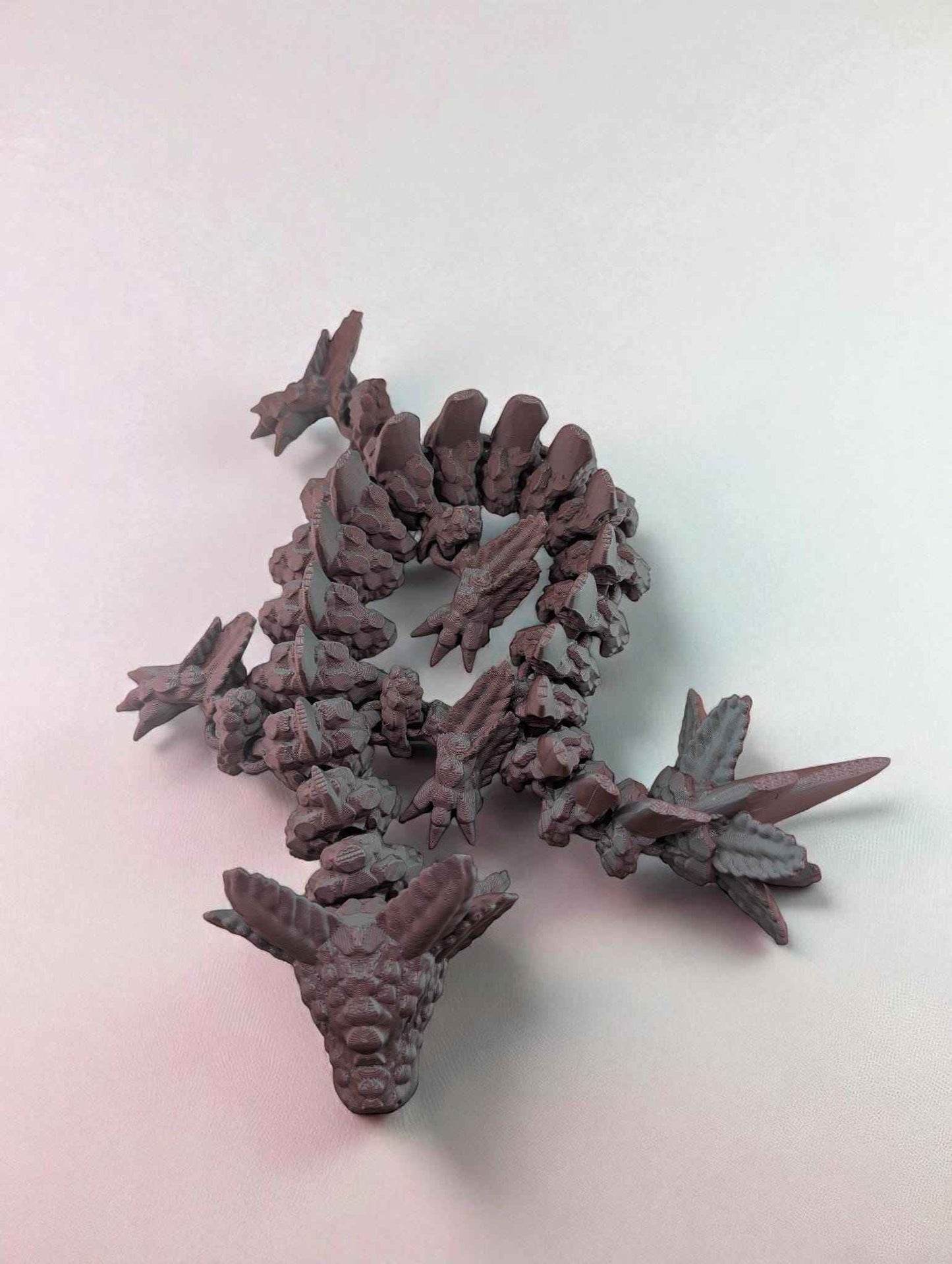Overhead shot of the textured matte articulated dragon coiled in an S-shape on a white surface.