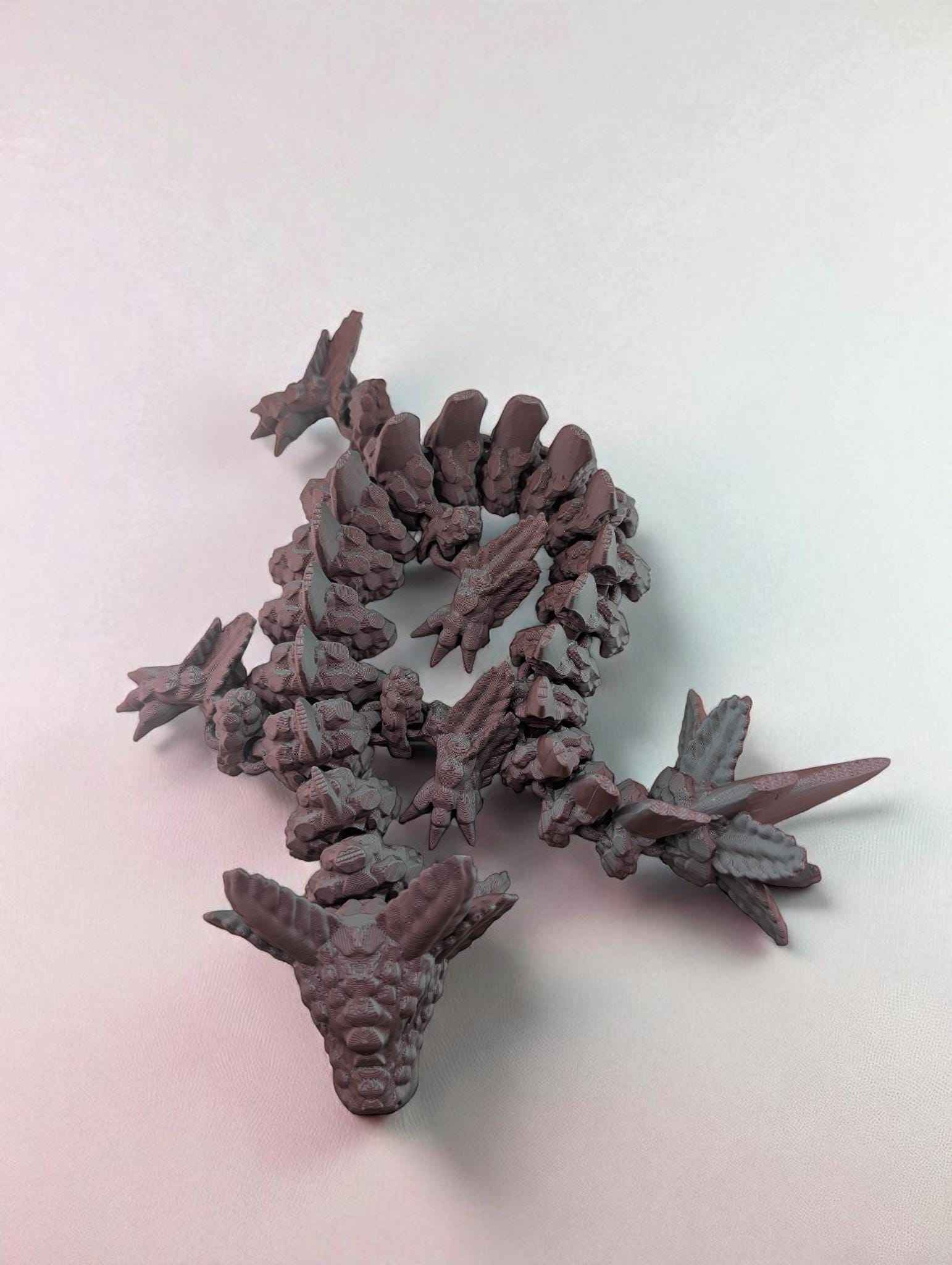 Overhead shot of the textured matte articulated dragon coiled in an S-shape on a white surface.