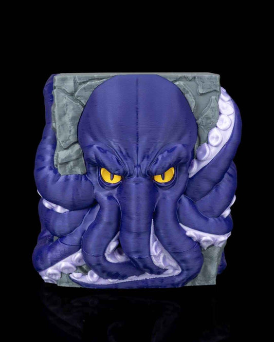 Full frontal view of a menacing, deep blue octopus head with bright yellow eyes, molded into a gray cracked stone wall.