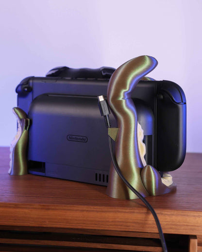Rear view showing the shimmering olive/bronze kraken stand cradling the console and routing a charging cable.